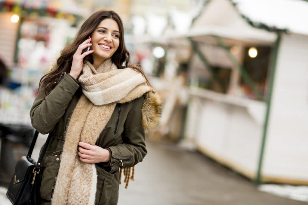 Woman walking in winter while on phone during the holidays smiling with her new dental crowns